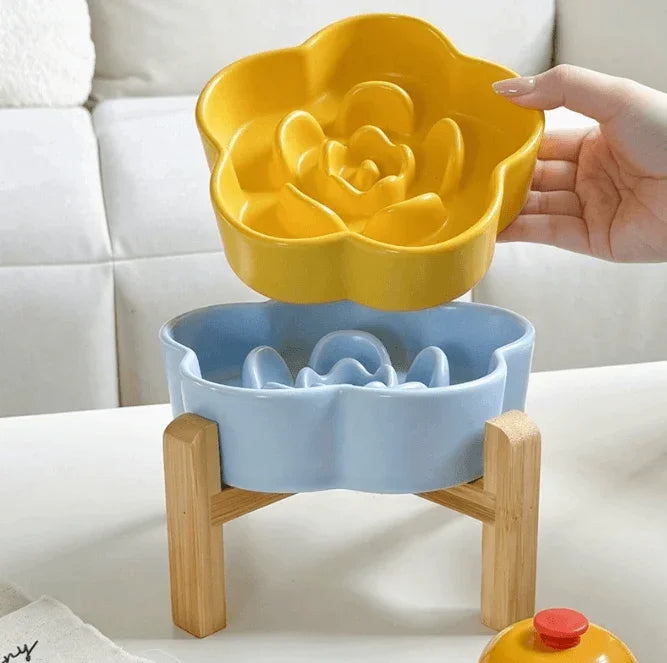 Yellow flower-shaped ceramic slow feeder bowl being lifted from a light blue base on a wooden stand.
