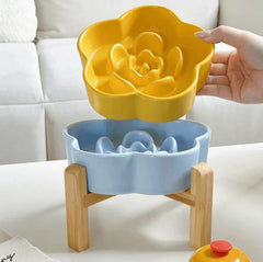 Yellow flower-shaped ceramic slow feeder bowl being lifted from a light blue base on a wooden stand.