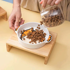 Cute cat-themed ceramic pet bowl with wooden stand, being filled with dry kibble for cats or small dogs