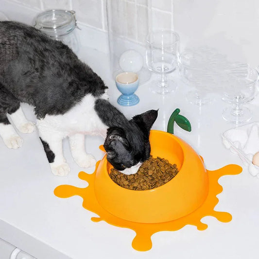 Cat eating from a yellow bowl with a green leaf design on a tiled bathroom floor.