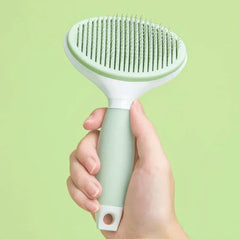 Michu Round-Head Grooming Dog Cat Brush in hand on a light green background.