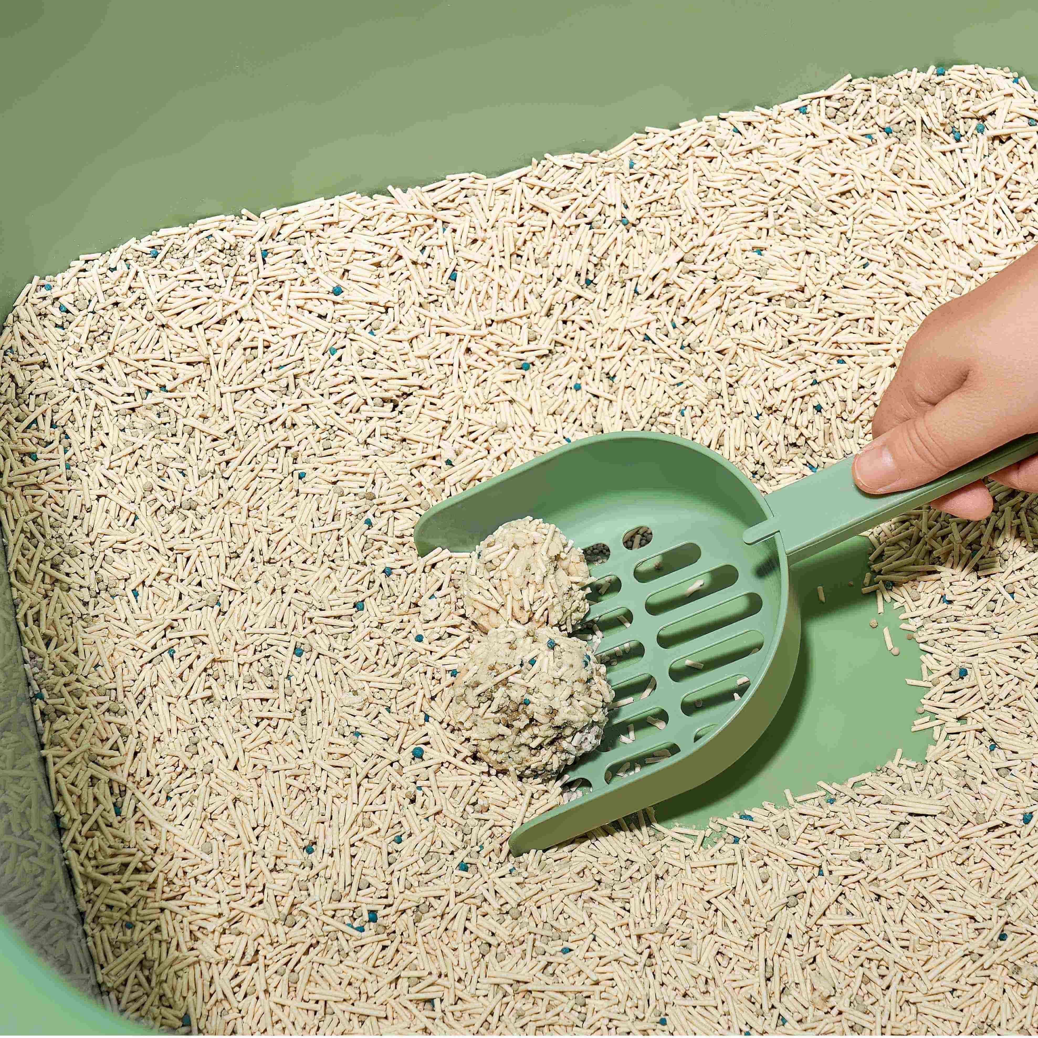 Green cat litter scoop scooping clumps from a litter box with pellet litter