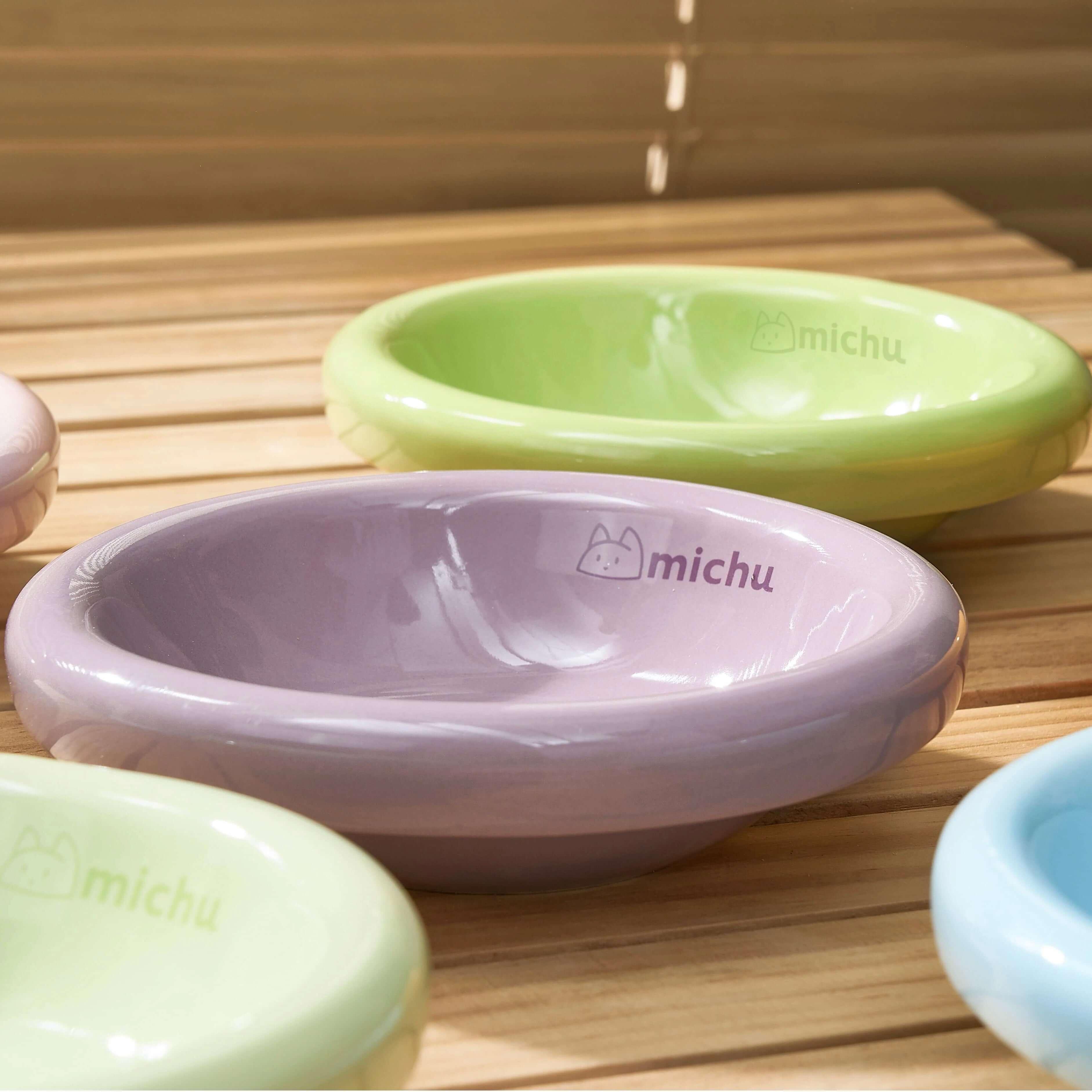 Michu Wide and Shallow Ceramic Pet Bowl in pastel colors on a wooden surface.