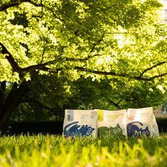 Three bags of cat litter on grass with trees in the background