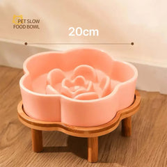 Pink flower-shaped ceramic slow feeder bowl by Petroom on a bamboo wooden stand.