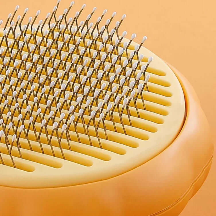 Close-up of a yellow pet grooming brush with metal pins on an orange background