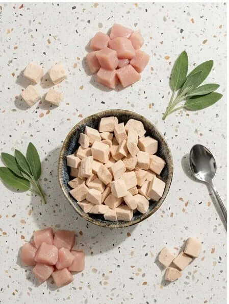PawDry Freeze-Dried Chicken Bites Pets Treat 100g displayed in a bowl with fresh herbs on a textured surface.