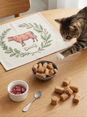 PawDry Freeze-Dried Beef Raw Meaty Bone (RMB) 100g with a cat exploring its meal on a decorated table.