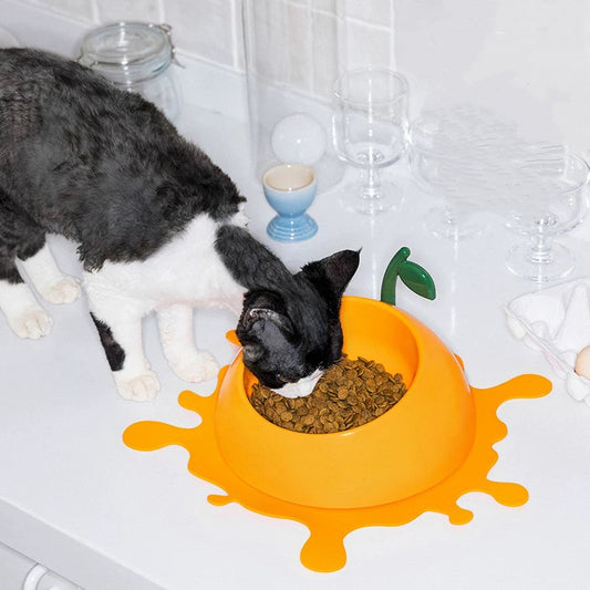 Cat eating from a yellow bowl with a green leaf design on a tiled bathroom floor.