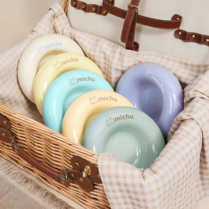Michu Ceramic Cat Bagel Bowl – Anti-Whisker Wide Shallow Pet Food Bowl Rainbow Colours displayed in a wicker basket.